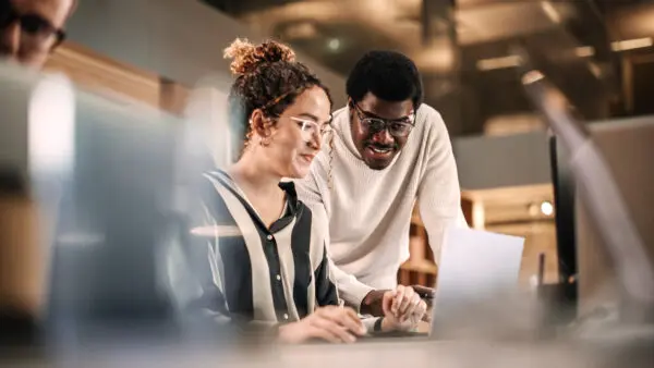 Two colleagues working together on a laptop in a modern office.